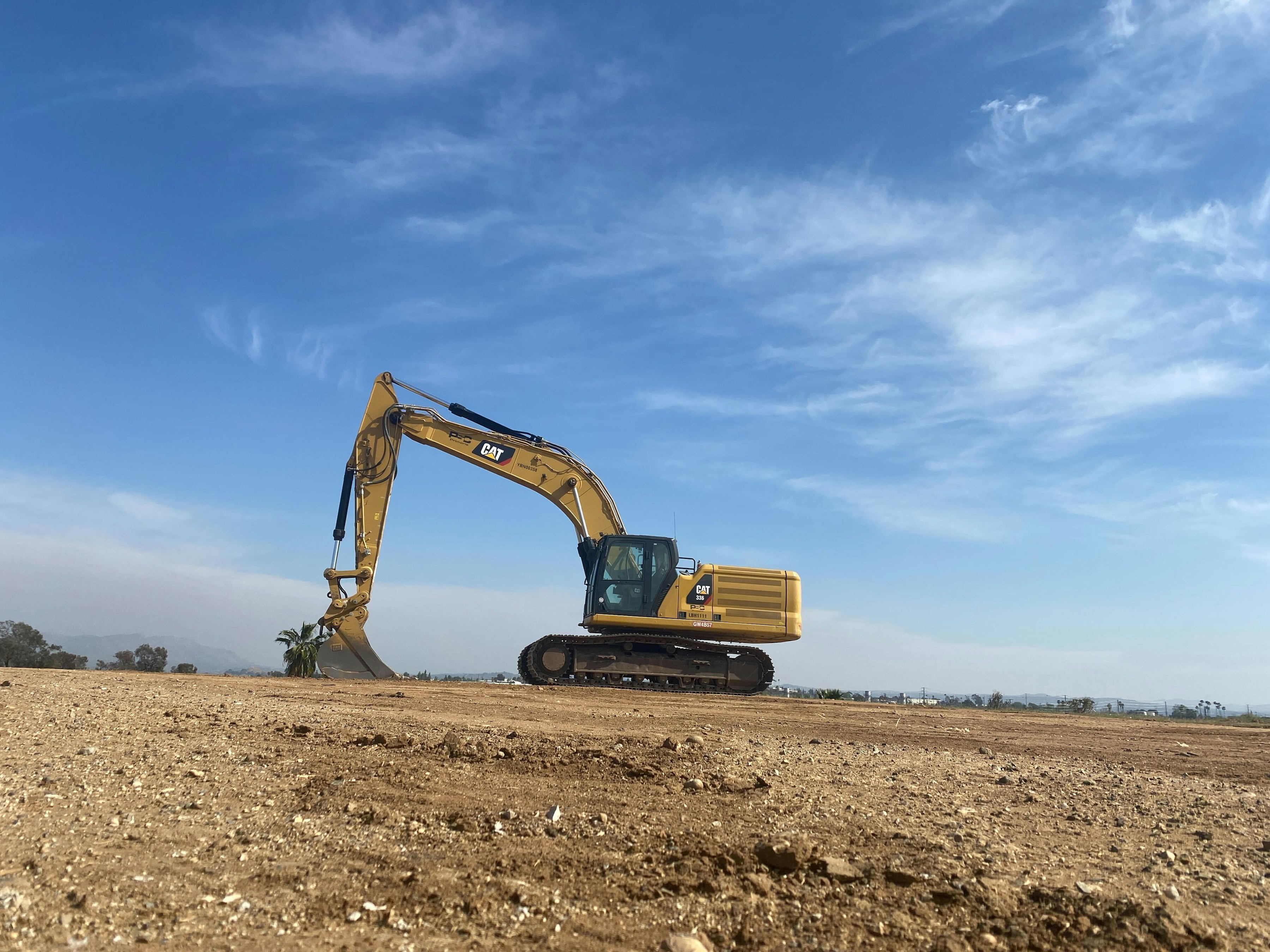 Photograph of a CAT excavator on a dirt site, with its raised boom extending above the image frame